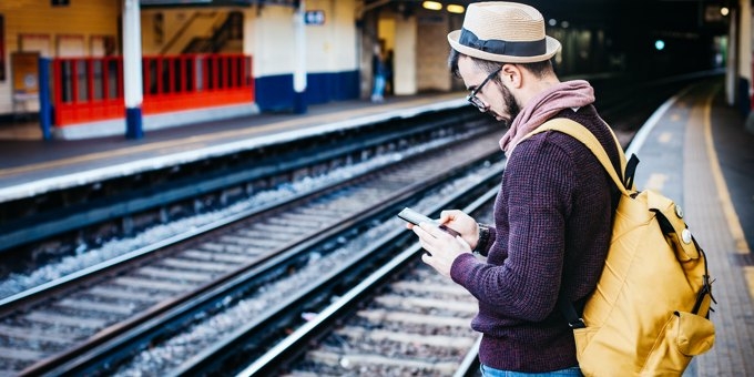 Man standing on station platform, browsing the web on his mobile phone